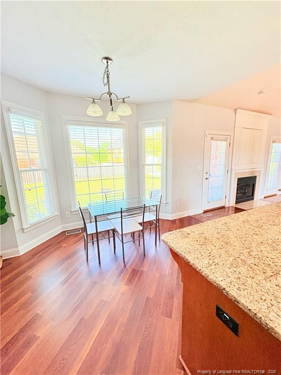 dining room with light wood-style flooring, baseboards, a chandelier, and a fireplace with flush hearth