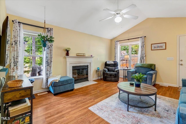 living room with a ceiling fan, light wood-type flooring, a fireplace, lofted ceiling, and baseboards