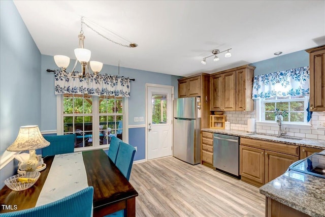 kitchen featuring appliances with stainless steel finishes, a sink, a chandelier, backsplash, and light stone countertops