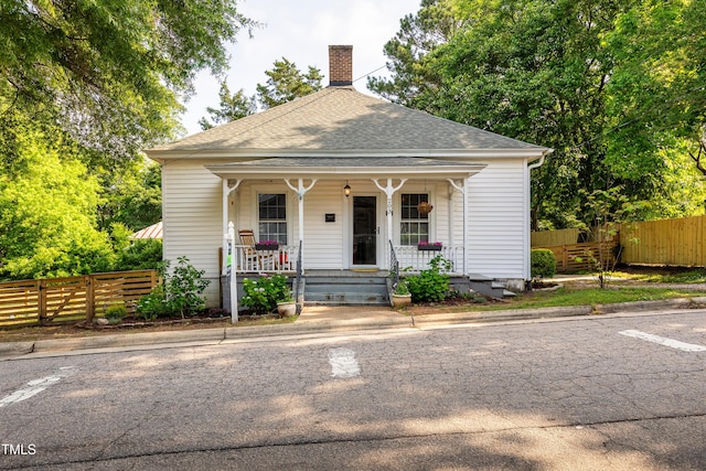 bungalow-style house featuring a shingled roof, covered porch, a chimney, and fence