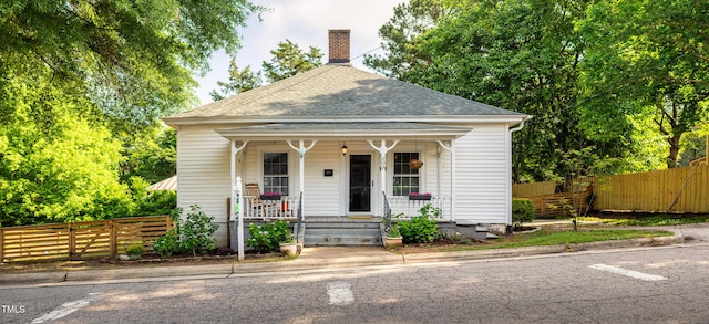 view of front of house featuring a porch, roof with shingles, and a chimney