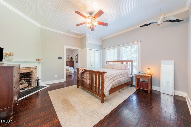 bedroom featuring crown molding, hardwood / wood-style flooring, a fireplace with raised hearth, baseboards, and a closet