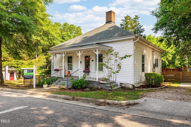 view of front facade featuring a chimney, fence, a porch, and a shingled roof