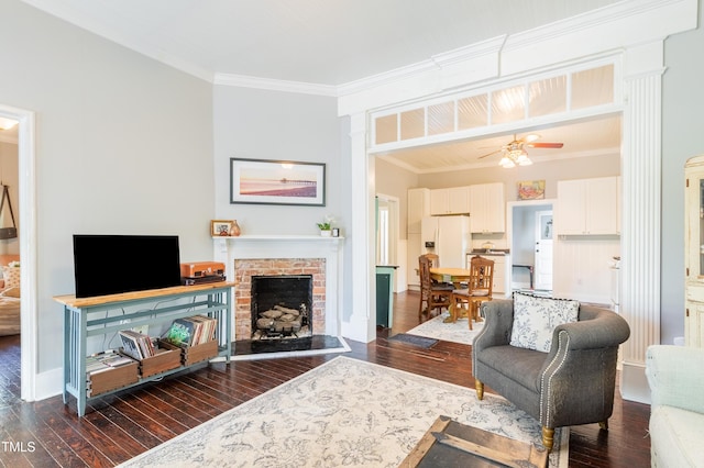 living room featuring dark wood finished floors, a brick fireplace, ceiling fan, ornamental molding, and baseboards