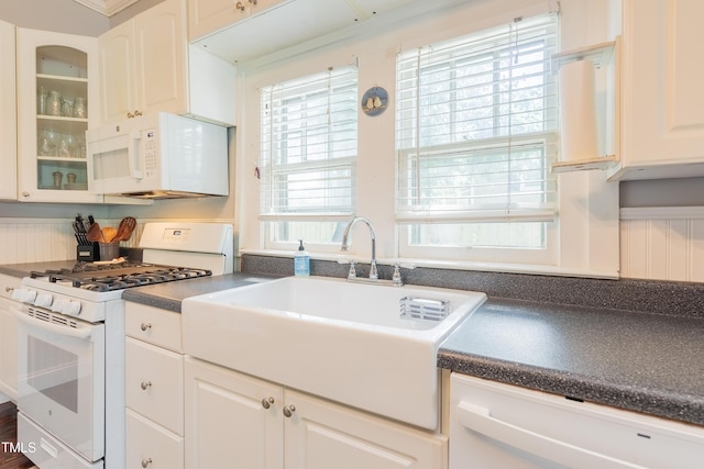 kitchen with white appliances, a sink, dark countertops, glass insert cabinets, and white cabinets