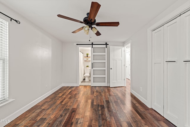 unfurnished bedroom with a barn door, hardwood / wood-style flooring, baseboards, and a closet