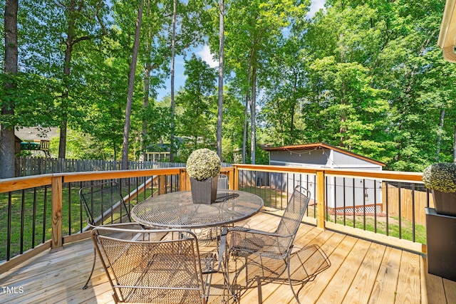 wooden terrace featuring outdoor dining area, a fenced backyard, an outbuilding, and view of scattered trees
