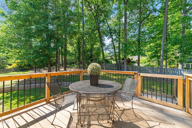 wooden terrace featuring outdoor dining area, a fenced backyard, and view of scattered trees