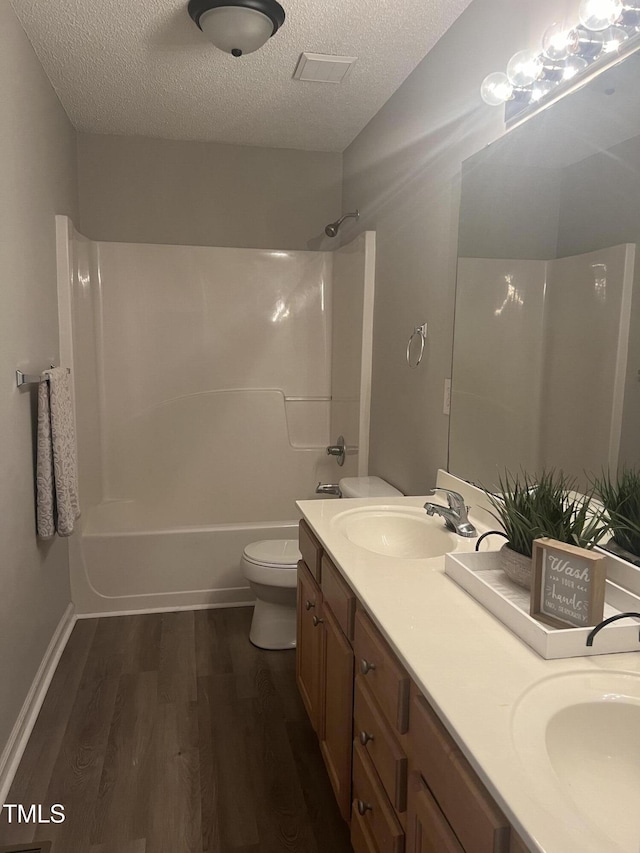 bathroom featuring a textured ceiling, wood finished floors, toilet, double vanity, and shower / tub combination