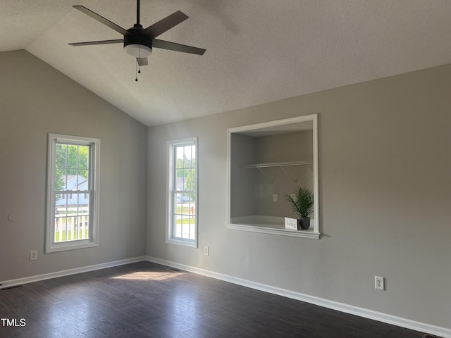 empty room featuring plenty of natural light, dark wood finished floors, baseboards, a textured ceiling, and vaulted ceiling
