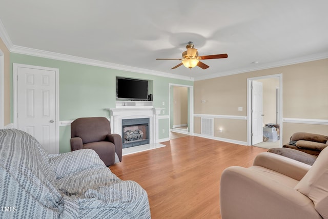 living room featuring crown molding, a ceiling fan, light wood-type flooring, and a fireplace