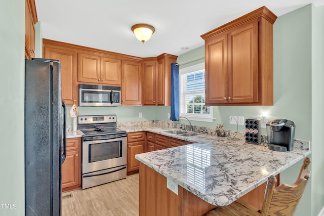 kitchen featuring appliances with stainless steel finishes, a sink, a peninsula, light stone counters, and light wood-style floors