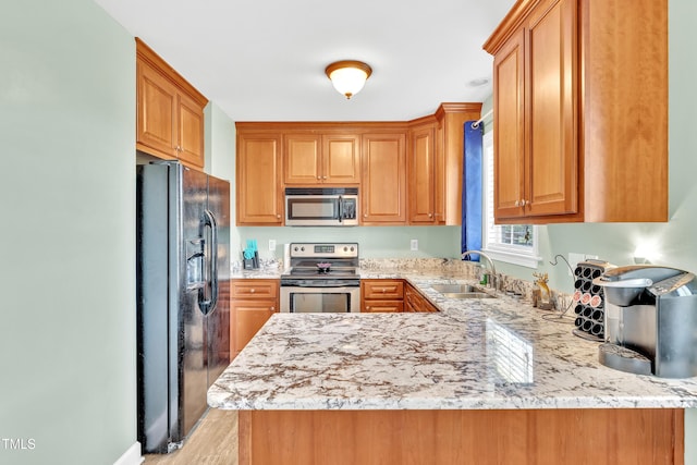 kitchen featuring appliances with stainless steel finishes, a sink, a peninsula, light stone countertops, and light wood finished floors