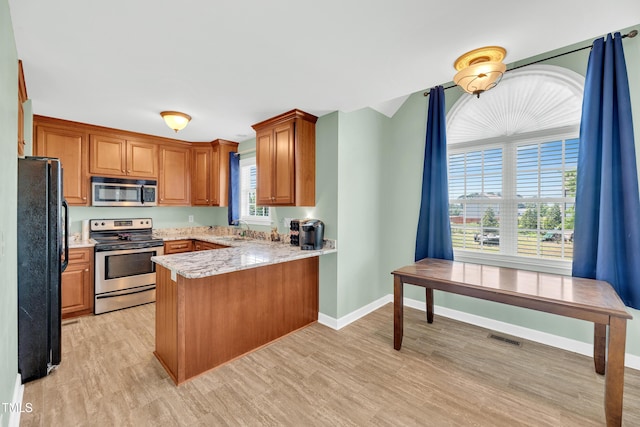 kitchen with stainless steel appliances, a peninsula, light wood-style flooring, and brown cabinets