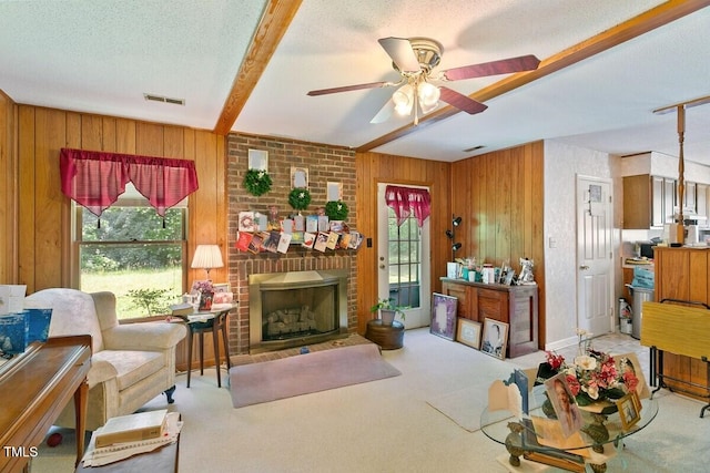 carpeted living room featuring plenty of natural light, wood walls, a ceiling fan, a textured ceiling, and a fireplace