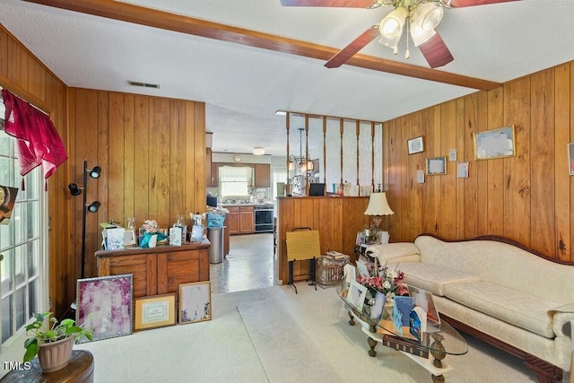 living area featuring wooden walls, a ceiling fan, and light colored carpet