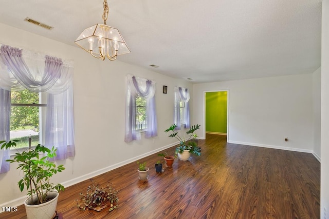empty room with a chandelier, wood finished floors, and baseboards