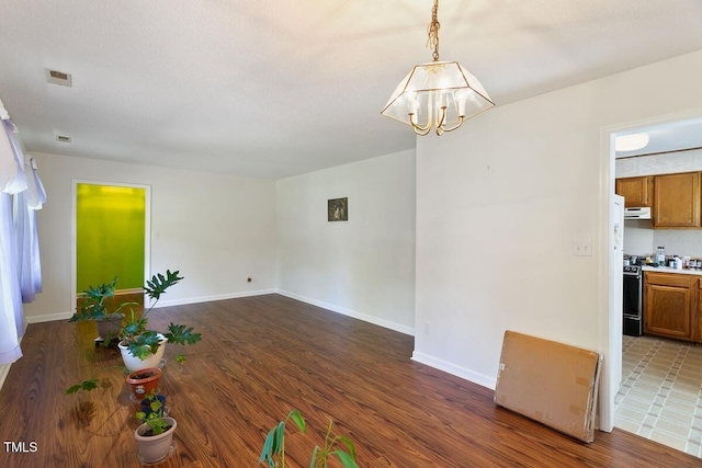 spare room featuring a chandelier, wood finished floors, and baseboards