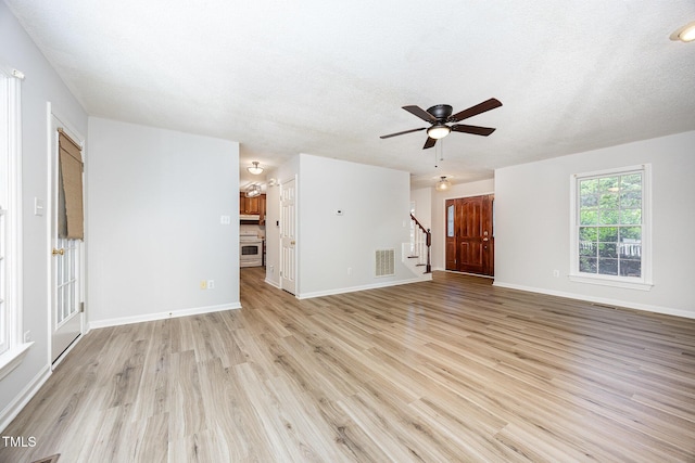 unfurnished living room with stairway, light wood-style flooring, ceiling fan, baseboards, and a textured ceiling