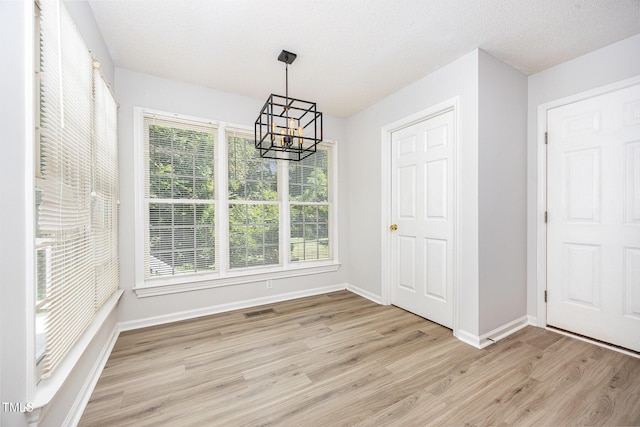 unfurnished dining area with a chandelier, light wood finished floors, and baseboards