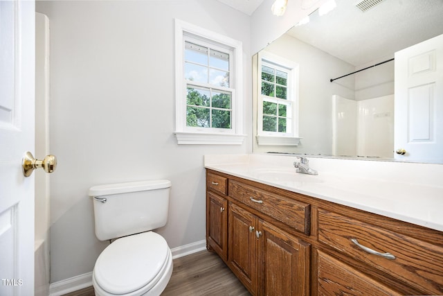 bathroom with baseboards, toilet, wood finished floors, vanity, and a shower