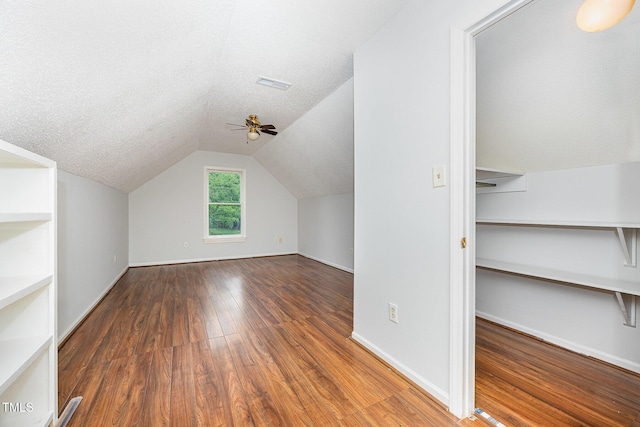 additional living space with ceiling fan, wood finished floors, lofted ceiling, baseboards, and a textured ceiling