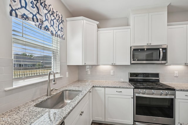kitchen with stainless steel appliances, a sink, tasteful backsplash, and white cabinets