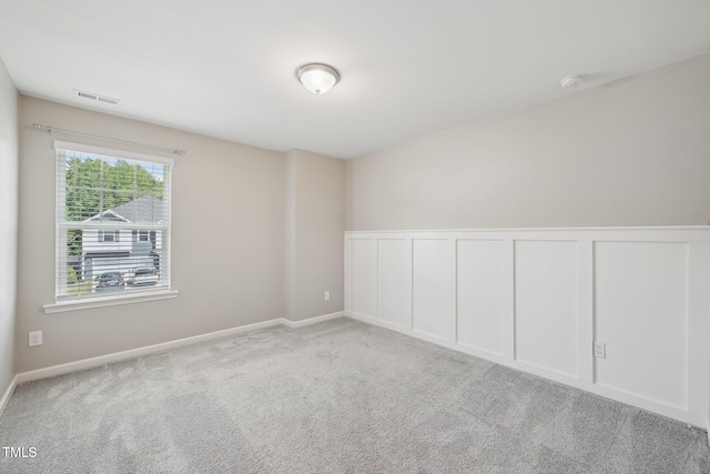 spare room with carpet, a smoke detector, a wainscoted wall, and a decorative wall