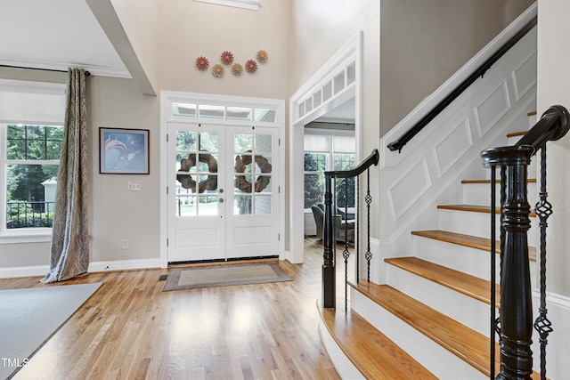entryway with stairs, light wood-style flooring, baseboards, french doors, and a high ceiling