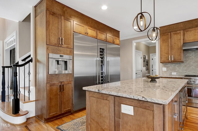 kitchen featuring premium appliances, light wood finished floors, light stone counters, crown molding, and backsplash
