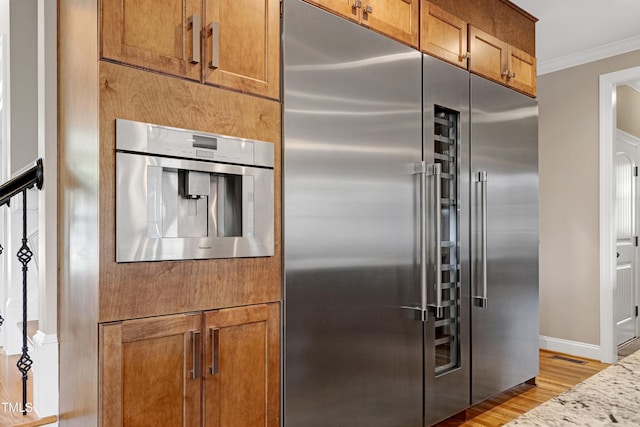 kitchen featuring built in fridge, ornamental molding, light wood-style flooring, brown cabinetry, and baseboards