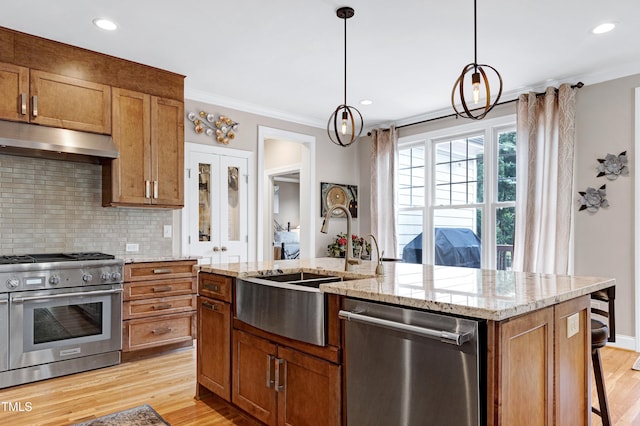kitchen with appliances with stainless steel finishes, under cabinet range hood, light wood-type flooring, crown molding, and tasteful backsplash