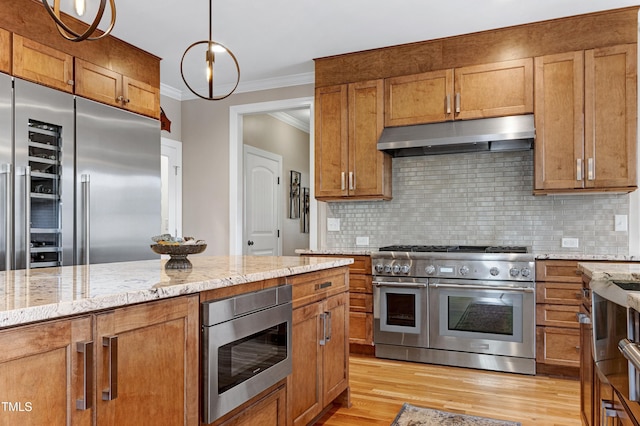 kitchen featuring built in appliances, under cabinet range hood, ornamental molding, light stone counters, and light wood-type flooring