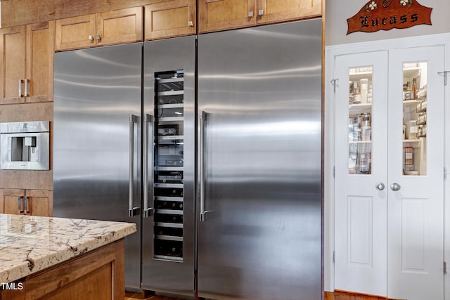 kitchen with stainless steel built in fridge, light stone countertops, and brown cabinets