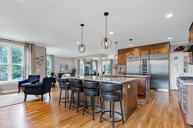 kitchen with a large island with sink, brown cabinets, light wood-type flooring, open floor plan, and recessed lighting
