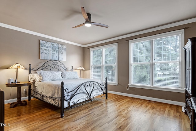 bedroom with baseboards, crown molding, wood finished floors, multiple windows, and a ceiling fan