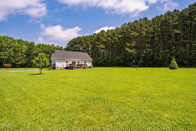 view of grassy yard featuring a wooded view and a wooden deck