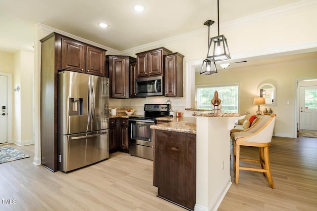 kitchen with appliances with stainless steel finishes, a peninsula, a kitchen breakfast bar, dark brown cabinets, and light wood-type flooring