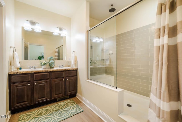 bathroom featuring a tile shower, wood finished floors, double vanity, baseboards, and tasteful backsplash