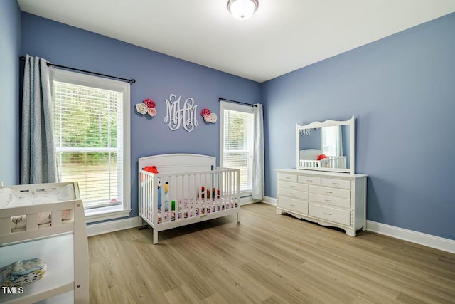 bedroom with light wood finished floors, baseboards, and a nursery area