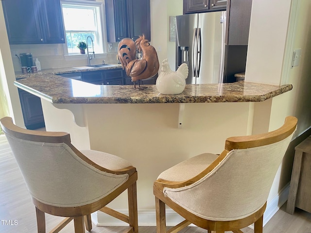 kitchen featuring a sink, stainless steel refrigerator with ice dispenser, blue cabinetry, light wood-style flooring, and a kitchen bar