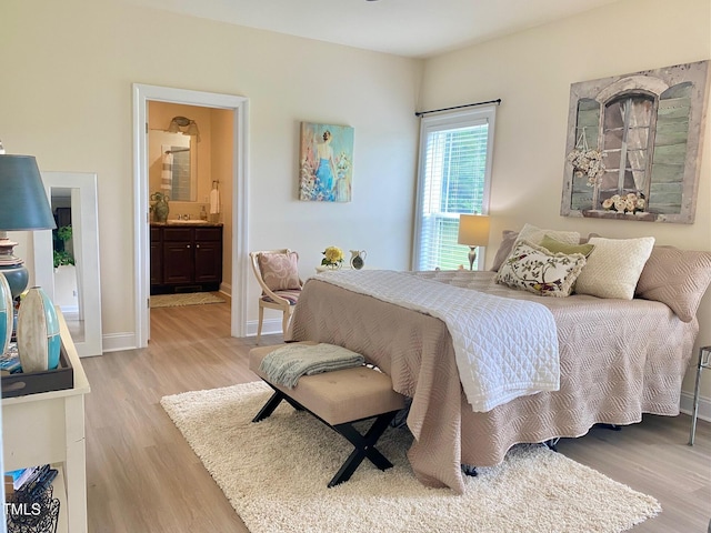 bedroom featuring light wood-style flooring, baseboards, and ensuite bathroom