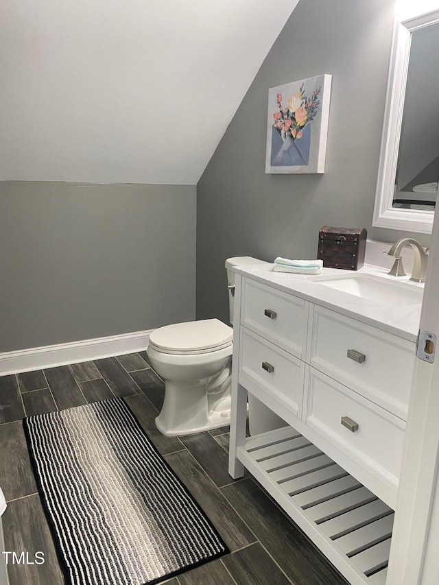 half bath with lofted ceiling, toilet, wood finish floors, vanity, and baseboards
