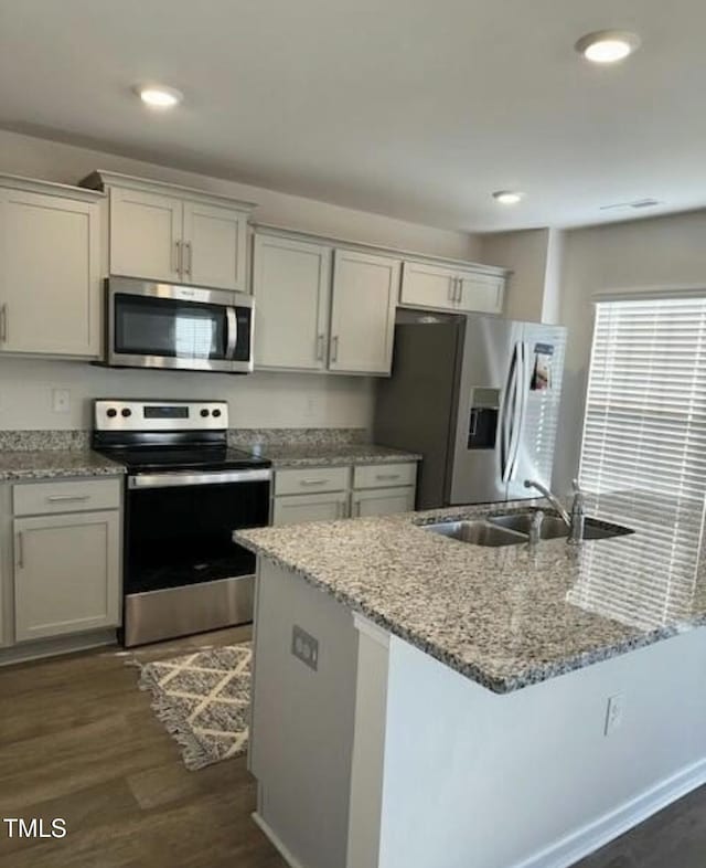 kitchen featuring stainless steel appliances, a sink, dark wood-style floors, light stone countertops, and recessed lighting