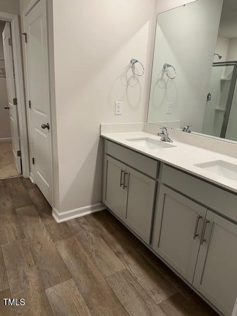 full bathroom featuring wood finished floors, double vanity, a stall shower, and baseboards