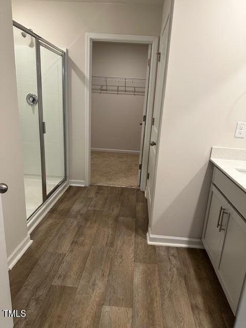 bathroom featuring a stall shower, wood finished floors, a spacious closet, vanity, and baseboards