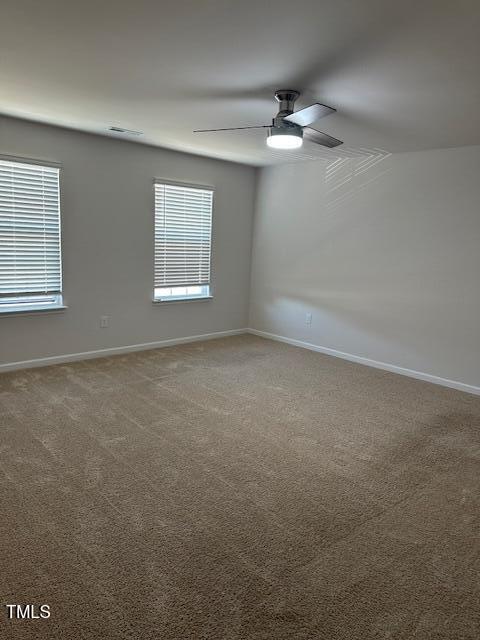 carpeted empty room with plenty of natural light, a ceiling fan, and baseboards