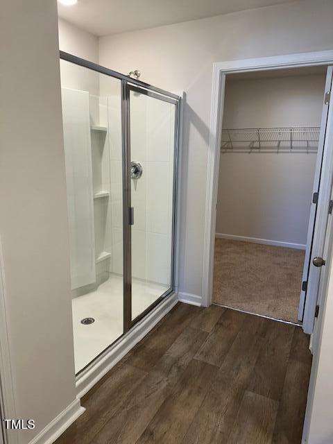 bathroom featuring a shower stall, wood finished floors, a spacious closet, and baseboards
