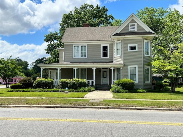 view of front of home featuring a porch, a chimney, and a front yard