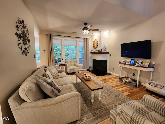 living area featuring wood finished floors, ceiling fan, a large fireplace, and baseboards